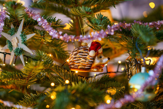 Close-up of Christmas ornament toys and balls hanging on a decorated tree with warm lights, festive tinsel and cozy holiday atmosphere at home.
