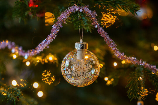 Close-up of Christmas ornament toys and balls hanging on a decorated tree with warm lights, festive tinsel and cozy holiday atmosphere at home.