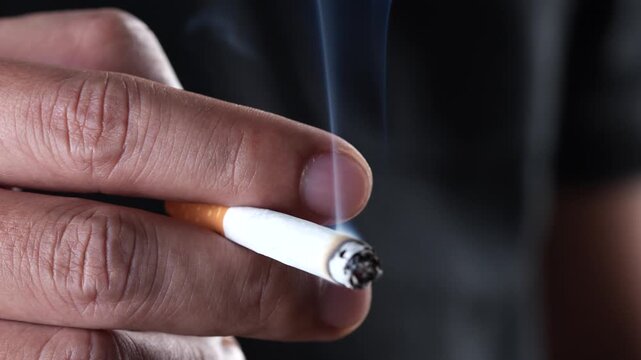 close up man holding smoking a cigarette in hand. smoke spread. dark background.