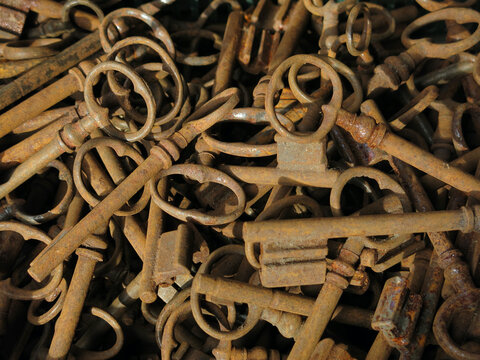 Pile of antique rusty skeleton keys background pattern. A close-up view of a large collection of old, rusty iron skeleton keys piled together, showing intricate metal details and natural rust texture.