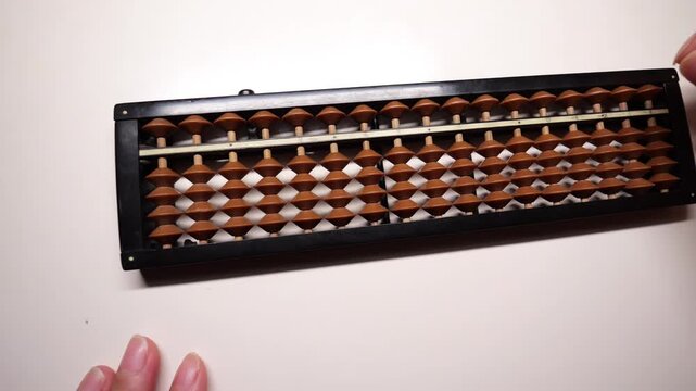 Hand using a wooden soroban abacus on white desk.