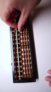 Hand using a wooden soroban abacus on white desk.