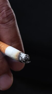 close up man holding smoking a cigarette in hand. smoke spread. dark background.