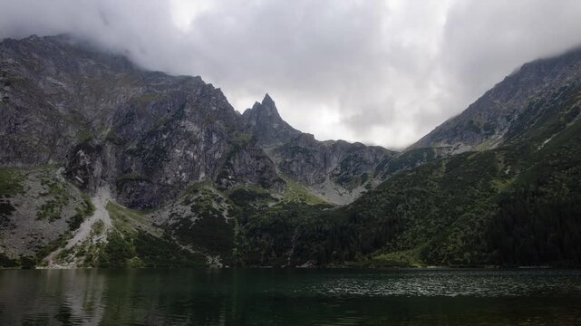 View of Morskie Oko lake surrounded by rocky peaks and lush greenery under a cloudy sky in Tatra County, Lesser Poland Voivode, Poland.