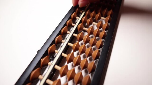 Hand using a wooden soroban abacus on white desk.