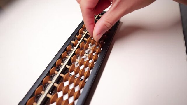 Hand using a wooden soroban abacus on white desk.