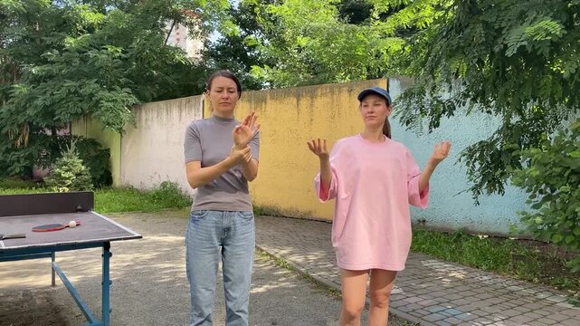 Two young women doing arm stretching exercises outdoors before playing table tennis