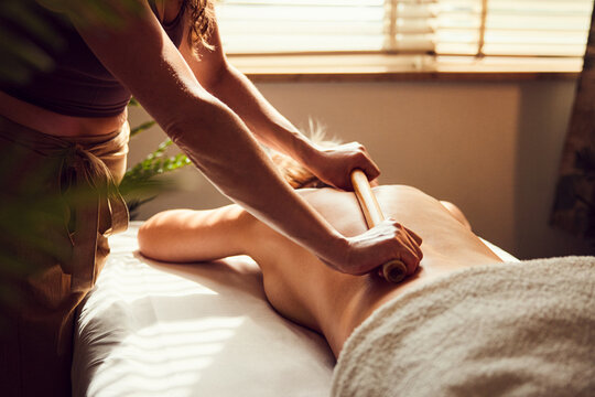 Therapist performing bamboo stick massage on woman's back at spa