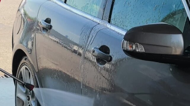 Car wash spraying soapy water on a modern vehicle exterior, auto detailing and vehicle maintenance concept