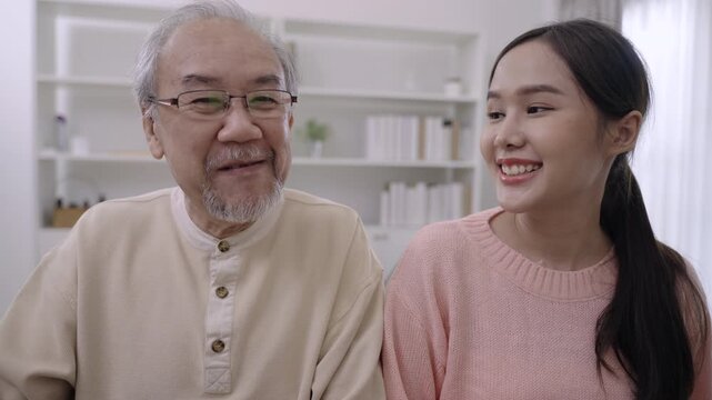 Happy beautiful Asian woman and her father are sitting smiling and playing piano, singing together having fun and cheerful in living room at home. Lifestyle and leisure after retirement with family. 