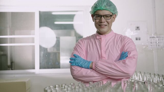 Happy Asian man technician inspector wearing glasses in a uniform of factory relaxing standing smiling with arms crossed while looking at the camera on a production line in the manufacturing industry.