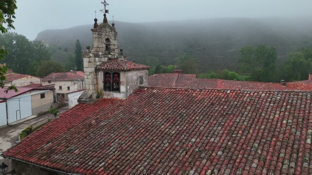 Aerial view descending towards Tosantos parish church in foggy rural Spain