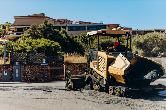 Asphalt paving machine working on a residential road during street resurfacing. Heavy construction equipment represents road renewal, infrastructure investment and municipal maintenance.