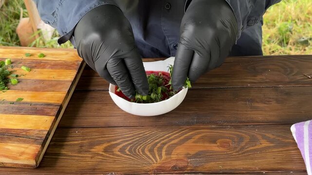 A person wearing black gloves pours chopped herbs into a plate of adjika,outdoor cooking. High quality 4k footage