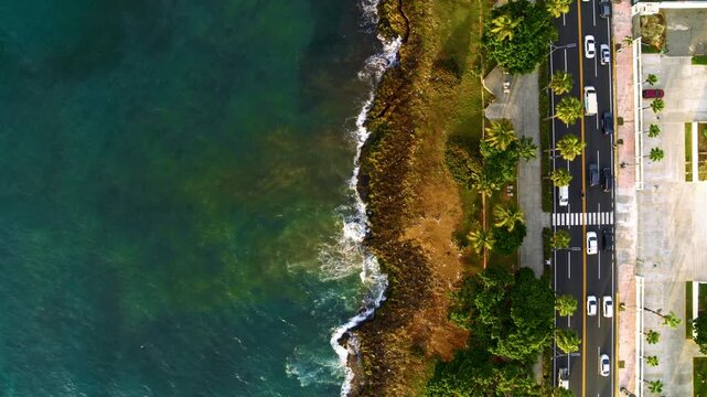 A high-angle view of a city thoroughfare and vehicles on the road. Road traffic is a vital part of infrastructure. An urban road running along the coastline. Sea surf.