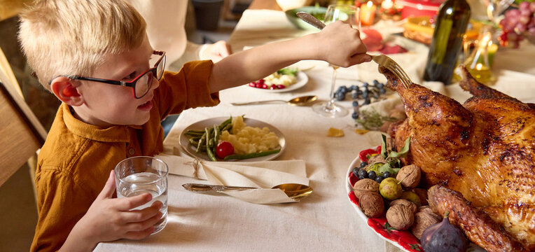 Young boy reaches toward Thanksgiving turkey at family table with eager delight. Childhood joy, holiday meal, family togetherness concept