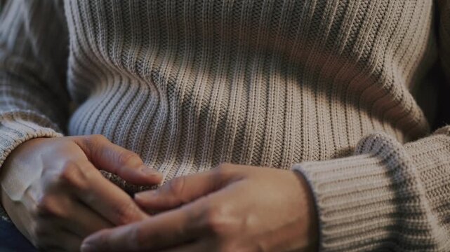 Noticing bandage, seated woman touching left knuckles and adjusting tape at home, beige sweater