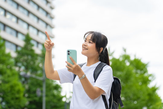 スマホを持って街を歩くアジア人観光客。アプリ、地図、マップ、道案内、インバウンド、AI、ナビ、旅行