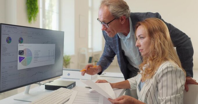 Senior manager explains investment allocation chart. Pointing with pencil at portfolio data. Daylight fills the room. Bright daylight. Concept of investment portfolio and risk management.