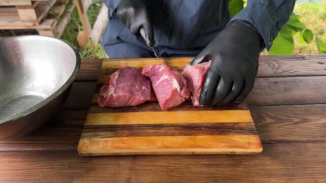 Close-up of a person in black gloves slicing meat on a wooden table outdoors. High quality 4k footage