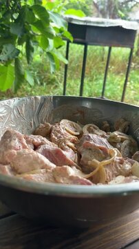 Close-up of marinated meat pieces in a metal bowl, with a barbecue grill in the background. High quality 4k footage