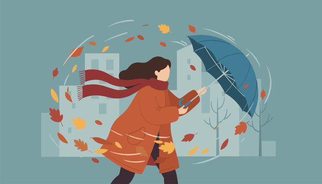 Woman wearing a warm coat and scarf walking through a strong autumn windstorm with swirling leaves and a blue umbrella.