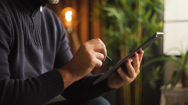 Male hands swiping up on tablet computer screen using digital stylus pen in office room, close up, slow motion