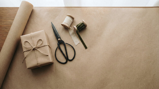 Gift wrapping station with brown paper, string and scissors on wooden table