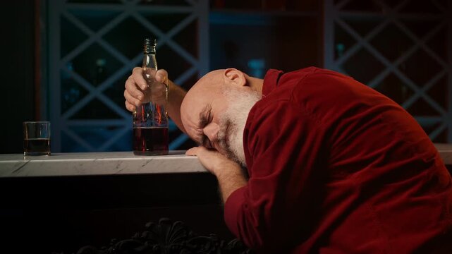 Middle-aged drunk man asleep with whiskey bottle at bar counter, alcoholism