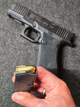 BALTIC STATES - SEPTEMBER 29, 2026: Hands holding a loaded Glock 19 Gen6 pistol magazine with brass 9mm cartridges, next to the handgun in a shooting range.