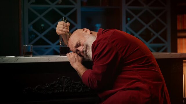 Drunk bearded man in his 50s asleep at bar counter with bottle, crisis