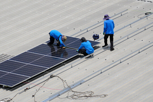 Skilled workers collaborate to attach solar panels to a metal framework on an expansive rooftop during a bright and sunny afternoon workday