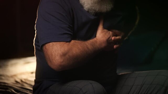 Middle-aged man holds chest while sitting on bed, heart failure warning