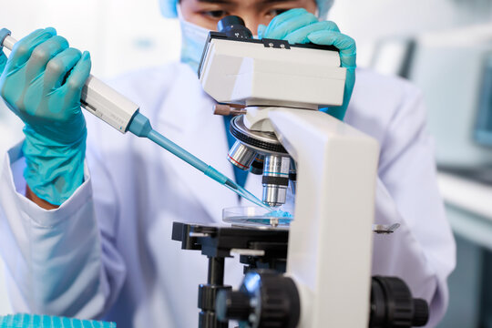 Close-up of a laboratory scientist in gloves using a pipette beside a microscope, preparing a slide for medical research and testing.