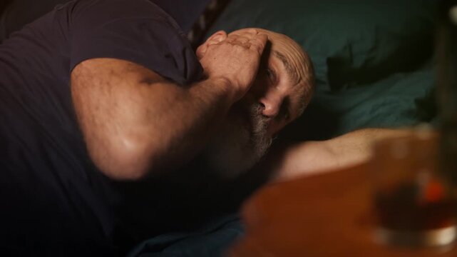 Bearded man in his 50s suffers bad hangover and holds head, alcoholism
