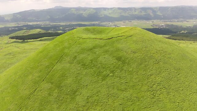 熊本県阿蘇の米塚を空撮、新緑の草原に覆われた火山地形と阿蘇谷の田園風景（Aerial view of Komezuka volcanic cone, Aso, Kumamoto, Japan）
