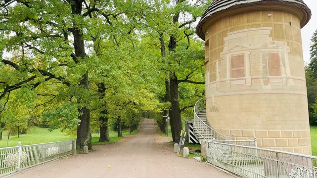 The historic Pil-Tower Pavilion stands quietly beside a tree-lined path in Pavlovsk Park, Saint Petersburg. This charming sight brings a serene feeling of wonder and nostalgia.