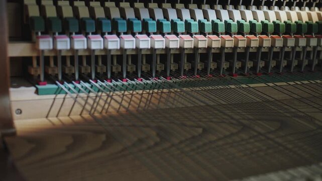 Moving camera revealing bank of metal strings over wooden soundboard inside piano, exposing jacks