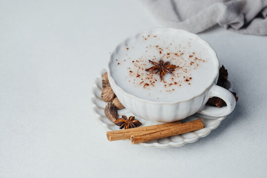 Cinnamon latte with frothy milk in a decorative cup with star anise and cinnamon sticks