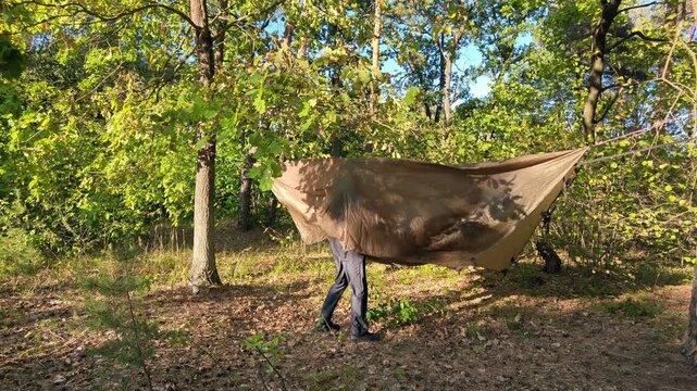 A camper organizes gear under a hanging tarp in the forest.