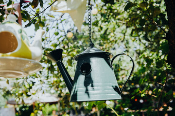 A watering can birdhouse hangs from a tree branch with greenery in the background © reddish