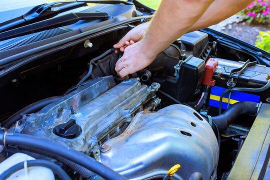 Car mechanic is fixing engine of car in driveway on tools, parts are nearby.