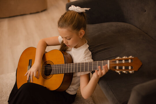 Focused child learning to play classical guitar during private music lesson at home