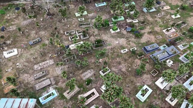 A view from above of a cemetery in Indonesia overgrown with weeds, featuring rectangular graves and a rusty shack.