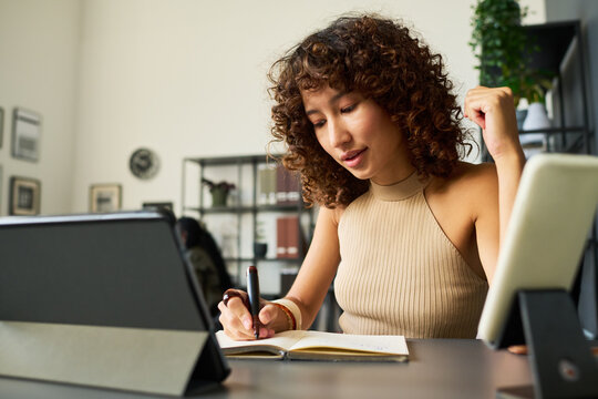 Young female designer writing in notebook while working with tablet in creative agency studio. Imagery suitable for digital marketing and branding campaign
