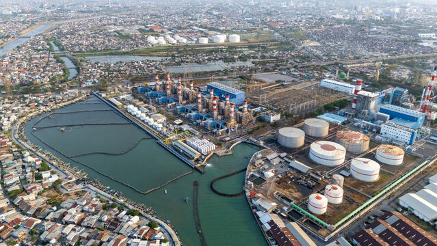 Aerial view of a large power plant facility with industrial storage tanks, chimneys, and surrounding urban infrastructure in Semarang, Central Java, Indonesia.