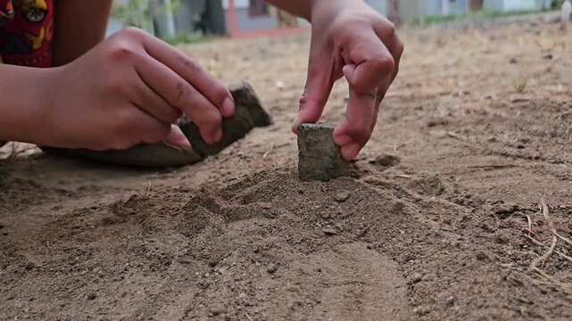 Child's hand playing with small stones and soil, exploring natural materials through tactile outdoor activity.