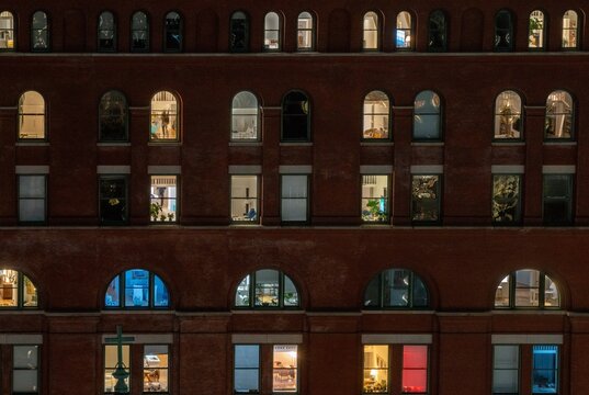 Aerial view of the illuminated facade of a brick office building at night, featuring rows of arched windows with warm and cool interior lighting, New York, New York, United States.