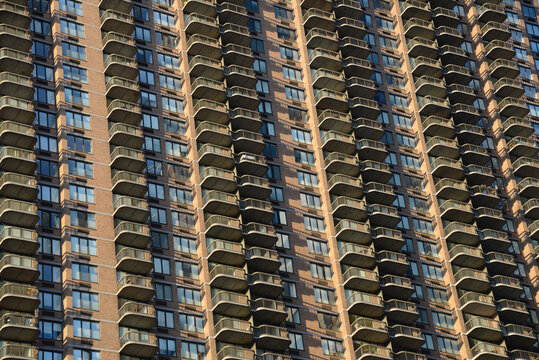 Aerial view of a high-rise office building facade featuring a repetitive pattern of balconies and windows under warm sunlight in New York, New York, United States.