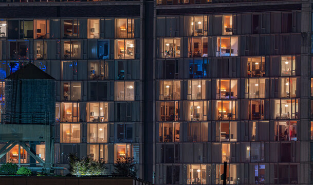 Aerial view of a modern high-rise office building facade at night with illuminated windows and a rooftop water tower in New York, New York, United States.